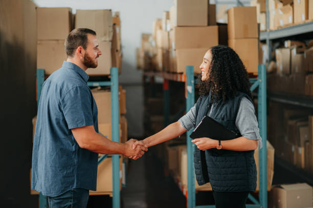 Shipping, supply chain and delivery partner with handshake for partnership, support and thank you in a warehouse. Box logistics or stock factory employee with teamwork, collaboration business meeting stock photo