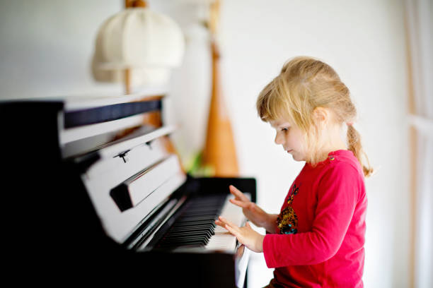 Beautiful little toddler girl playing piano in living room. Cute preschool child having fun with learning to play music instrument. Early musical education for children. stock photo