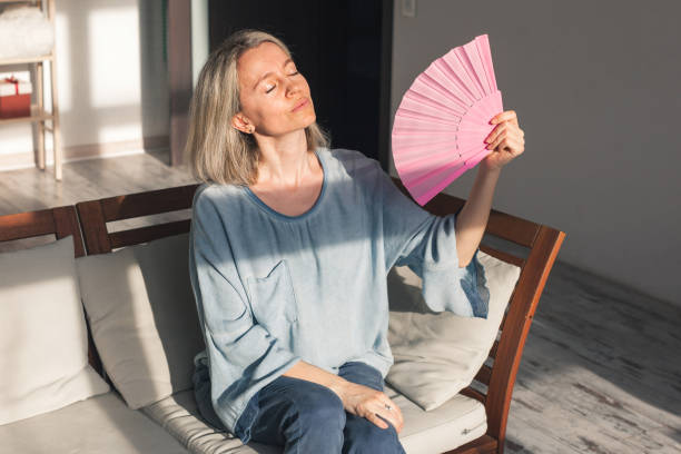 istock Exhausted middle aged woman using paper waver, suffering from hot summer 1425557901