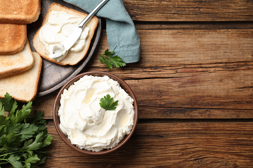 Toasted bread and delicious cream cheese with parsley on wooden table, flat lay. Space for text
