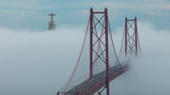 Aerial view 25 de Abril Bridge, Lisboa, covered in fog with several transports from one side to the other