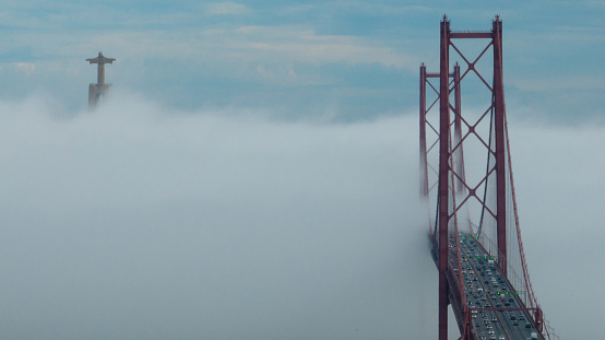 Aerial view 25 de Abril Bridge, Lisboa, covered in fog with several transports from one side to the other