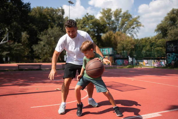 Father and son at public basketball court playing basketball. stock photo