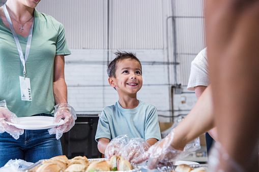 The elementary age boy works with his family at the volunteer event to help serve food.