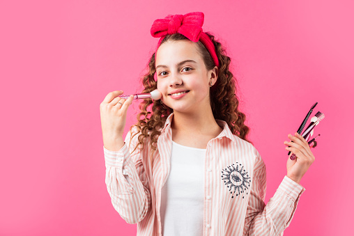 impose blush on cheeks. retro girl put natural makeup with brush. hair and skin care. small girl wear vintage headband. beautiful kid play cosmetics. Beauty salon. happy childhood. fashion and beauty.