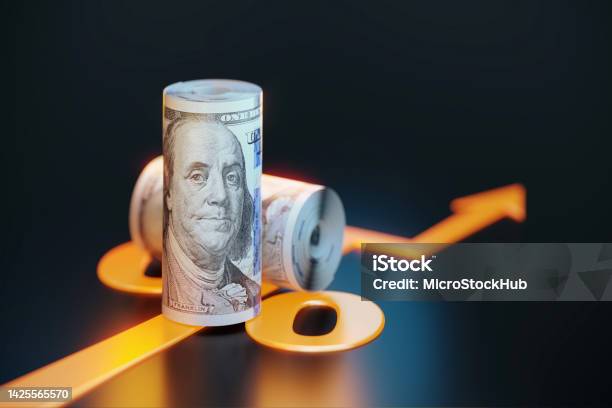 Rolled Up 100 American Dollar Bills Sitting Over Orange Colored Arrow Symbol On Black Background Stock Photo - Download Image Now