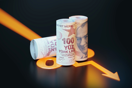 Rolled up 100 Turkish Lira bills sitting over orange colored arrow symbol sitting on black background. Horizontal composition with copy space. Finance concept.