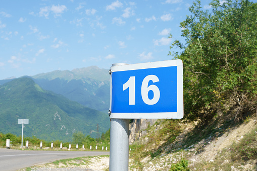 Sign limiting the speed of movement to 30 miles per hour of measurement on a street lighting pole, close-up shooting from a distance and with the perspective of the roofs of houses in blue sky.