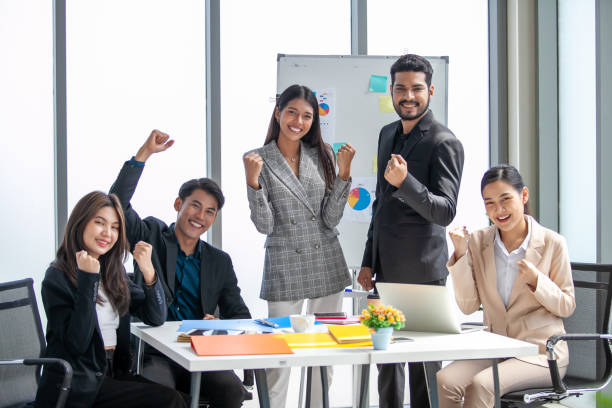 el equipo de negocios asiático celebra la victoria corporativa juntos en la oficina, riendo y regocijándose, sonriendo emocionados empleados colegas gritando de alegría en la oficina. - líderes jóvenes fotografías e imágenes de stock