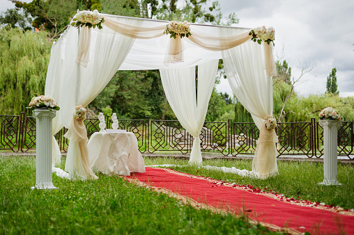 Wedding white arch decorated with flowers in the garden.