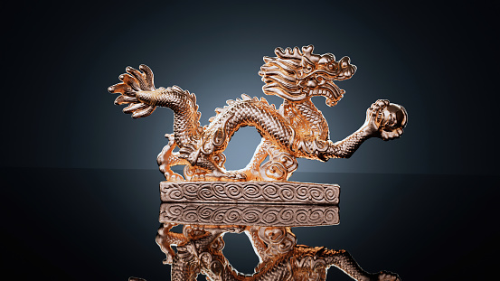 Golden dragon statuette in a professional lightening isolated on a dark background for a posh design. Gold Chinese dragon figure in a black background for a great screensaver