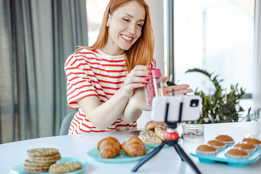 Young woman showing cake decoration products while vlogging at home