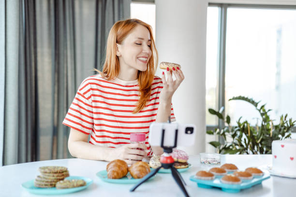 giovane donna che mangia dolci e filma vlog per i social media - muffin blueberry muffin blueberry food foto e immagini stock