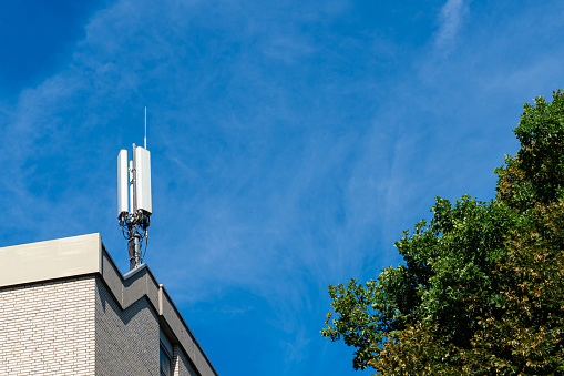 Broadcasting antenna on the roof of the administrative building. Blue sky with light white clouds and tree crown.