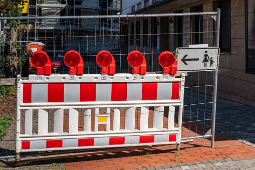 Red and white portable plastic barrier with red signal lights prohibiting entry to construction site.