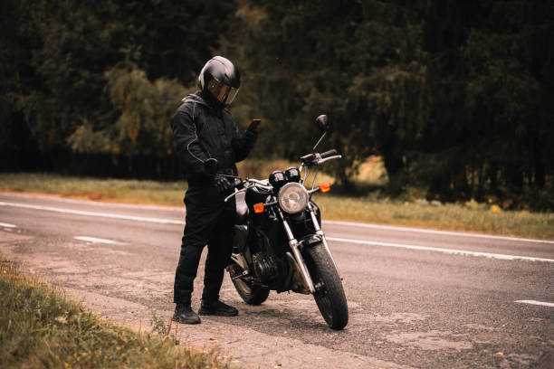 male biker motorcyclist holding a smartphone in gloves in autumn on a motorcycle on a journey. stock photo