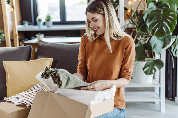 istock Smiling young woman unpacking parcel while sitting on couch at home 1425594688