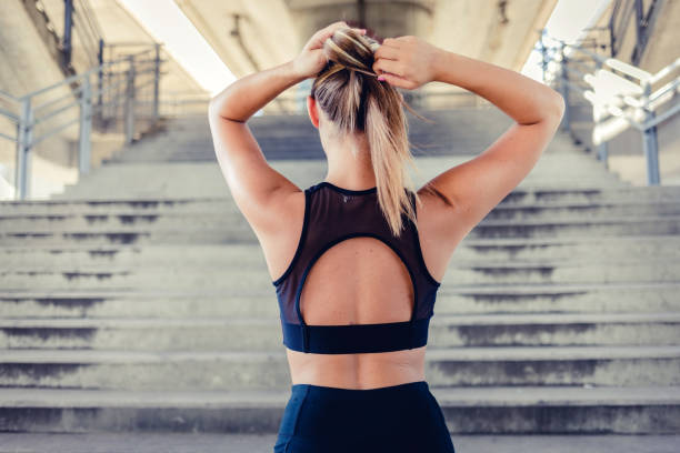 I don't want my hair getting in the way. Rear view photo of a cute female person making her ponytail while getting ready for workout during the day. Young woman getting ready for training. woman tying hair in ponytail getting ready for exercising stock pictures, royalty-free photos & images