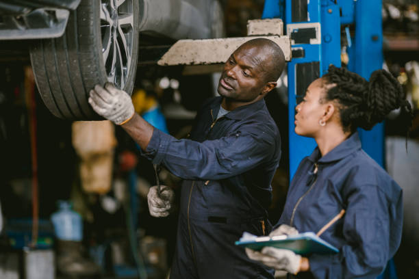 Auto garage worker Black African working together to fix service car vahicle wheel support together stock photo