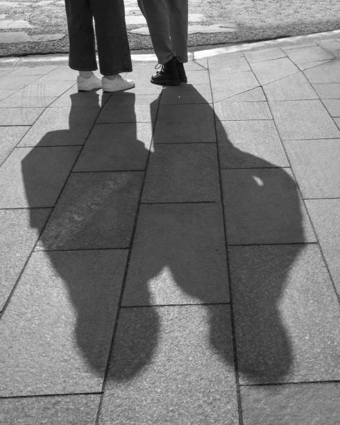 istock Shadows of 2 people and legs on tiled pavement outdoors. Black and white. 1425618421