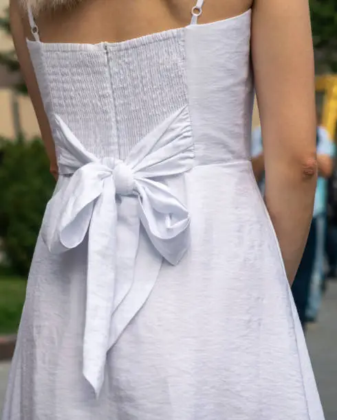 Woman's back wearing white dress with big bow knot. Street fashion