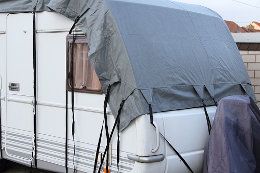 A caravan is winterized with a gray weatherproof tarpaulin