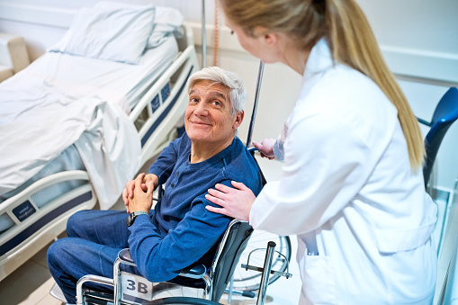 Smiling senior patient sitting on wheelchair looking at doctor consoling in hospital