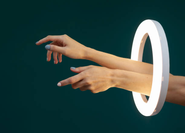 istock Female hands with a beautiful manicure through a glowing circle ring lamp on a green background 1425624422