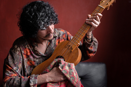 A young Mexican musician is cleaning his jarana guitar. Concept of composing music at home