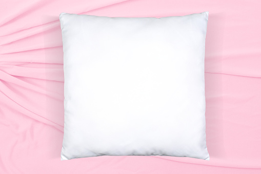 Top view of square white throw pillow napping atop a soft pink background.
