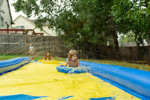 Ethnic group of young siblings playing in their backyard on a slip and slide. They are enjoying summer adventures together!