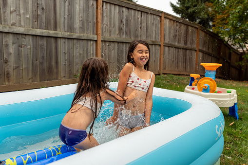 Young Latin American siblings are playing in their backyard inflateable pool. They are happy and enjoying summer and sunshine while splashing one another.