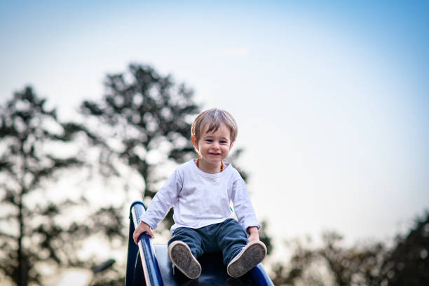 A happy toddler boy looking down sliding down slide at playground at sunset