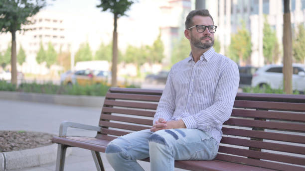 istock Young Adult Man Looking Around while Sitting on Bench Outdoor 1425640493