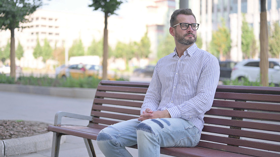 Adult Man Looking Around while Sitting on Bench Outdoor