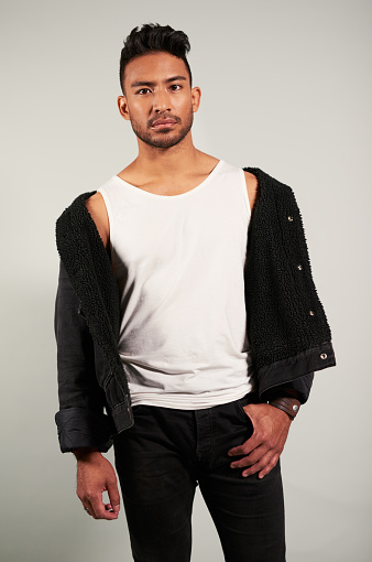 Portrait of a stylish, fashion and cool model standing in a studio with a gray background. Young, confident and serious indian man in a handsome, edgy and casual and outfit or clothes.