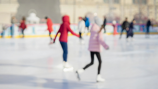 Blurred abstract winter background. Teenagers girlfriends ice skating in city park