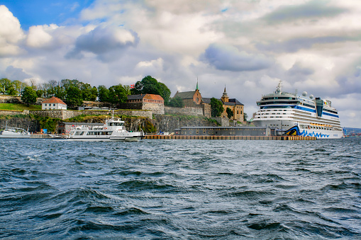 Oslo, Norway 0 August, 2019: Akershus Fortress/ Castle and  the AIDA Luna cruise ship in the harbor of Oslo. The castle was built around somewhere in the 1290's by King Haakon V. It has  functioned as a prison and a military base, currently it's also temporary housing for the Prime Minister.