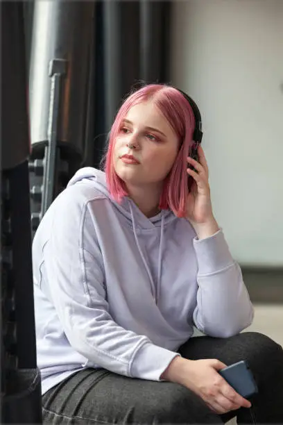 Portrait of an attractive young caucasian woman with pink hair listening to music with headphones