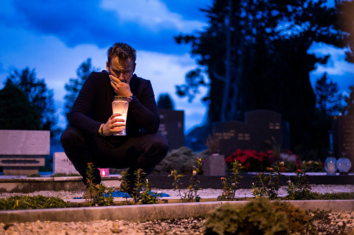 Man is lighting a candle. There are a lot of grave candles in a row. There are some flowers in the background.