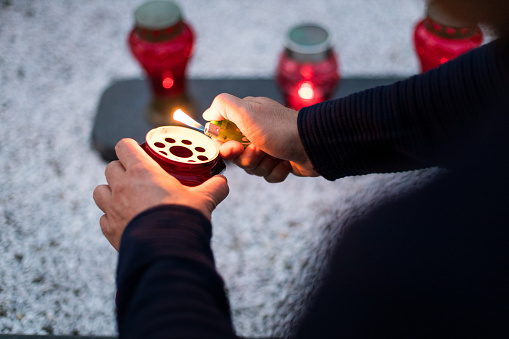 All Saints' Day and christian hands with candle light of memory on cemetery