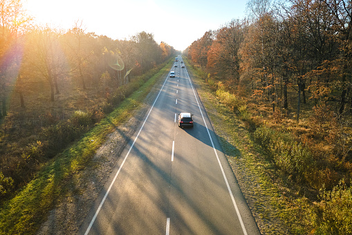 Aerial view of intercity road with fast driving cars between autumn forest trees at sunset. Top view from drone of highway traffic in evening.