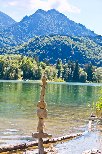 Stone tower on a lake in the Bavarian Alps, Germany. In mountain regions, stone towers are landmarks for hikers. In ancient Greece, stone towers represented the cult image of Hermes, the god of the way. In Scandinavia you are protected from trolls if you place a stone on an existing stone tower or cairn.