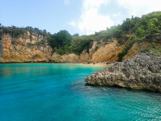 Long shot of the stunning reef cliff coastline of Curacao, featuring turquoise waters, wild vegetation along the coast, and a vast sky filled with swirling clouds.