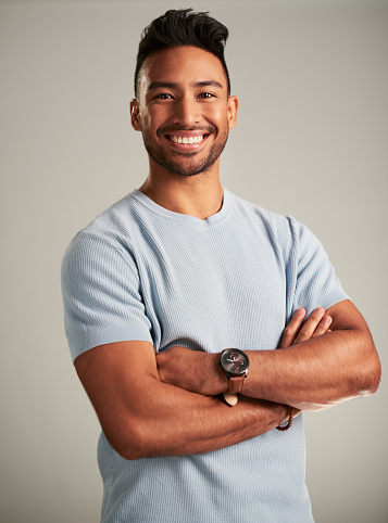 Portrait of a happy Indian man with a smile standing with his arms crossed in a studio. Attractive, confident and young male model with a joyful, happiness and positive lifestyle by a gray background