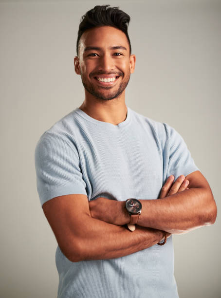 Portrait of happy, attractive and positive man with a smile standing with his arms crossed in studio. Confident, joyful and young male model with a happiness and positive lifestyle by gray background Portrait of a happy Indian man with a smile standing with his arms crossed in a studio. Attractive, confident and young male model with a joyful, happiness and positive lifestyle by a gray background charming stock pictures, royalty-free photos & images