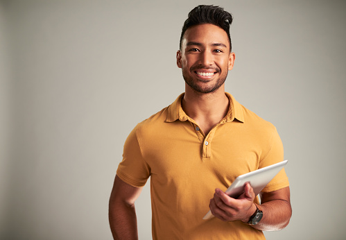 Portrait of man with smile and tablet against a grey studio mockup background. Young happy and cheerful male university student with digital technology for online research with project or assignment