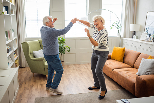 Senior couple at home listening music and dancing in living room.