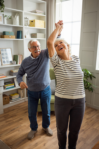 Senior couple at home listening music and dancing in living room.