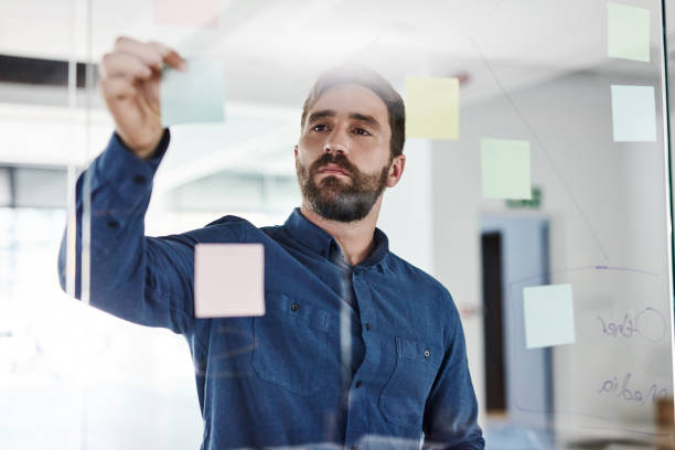 istock Business man planning company growth strategy and development using sticky notes in an office. Serious male entrepreneur working on a marketing plan or startup mission or vision at the workplace 1425669838